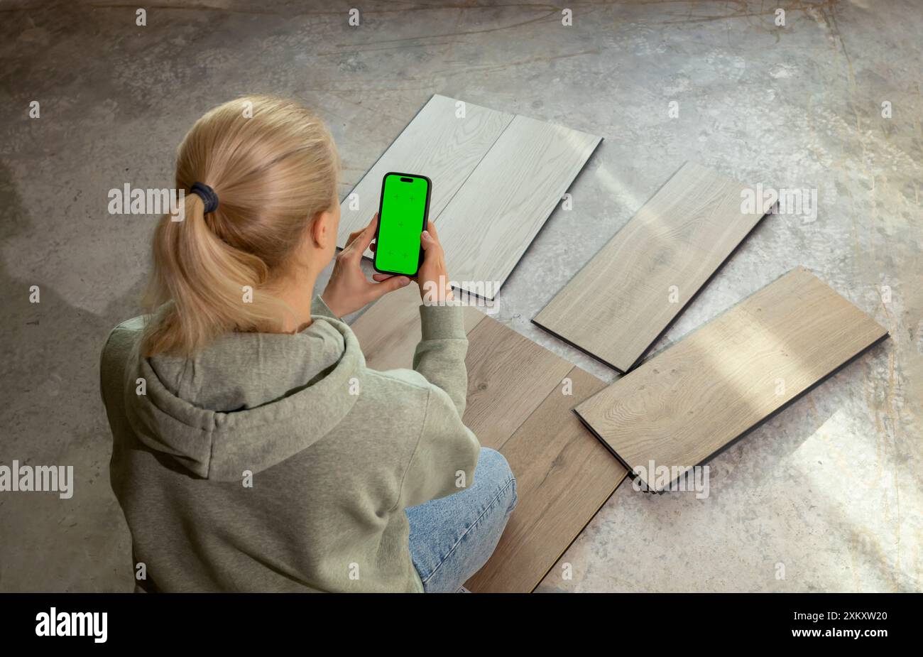 Designer d'intérieur tient smartphone avec l'écran de clé Chroma vert au-dessus des échantillons de bois de vinyle de luxe sur le plancher de béton dans la maison. Choix, sélection Banque D'Images