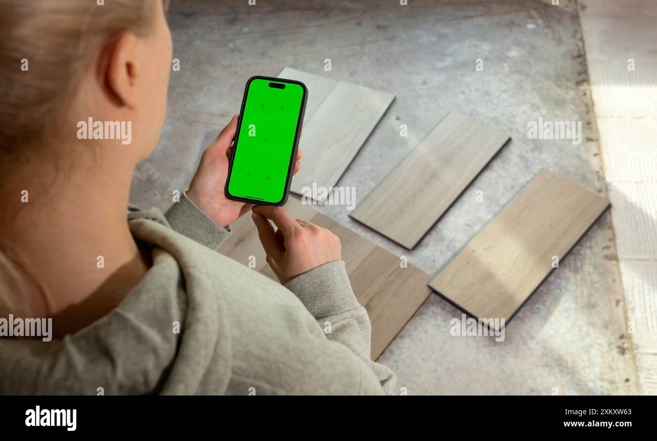 Designer d'intérieur tenant dispositif avec écran à clé Chroma vert au-dessus des échantillons de bois de vinyle de luxe, stratifié sur le sol dans la maison. Choix, sélection Banque D'Images