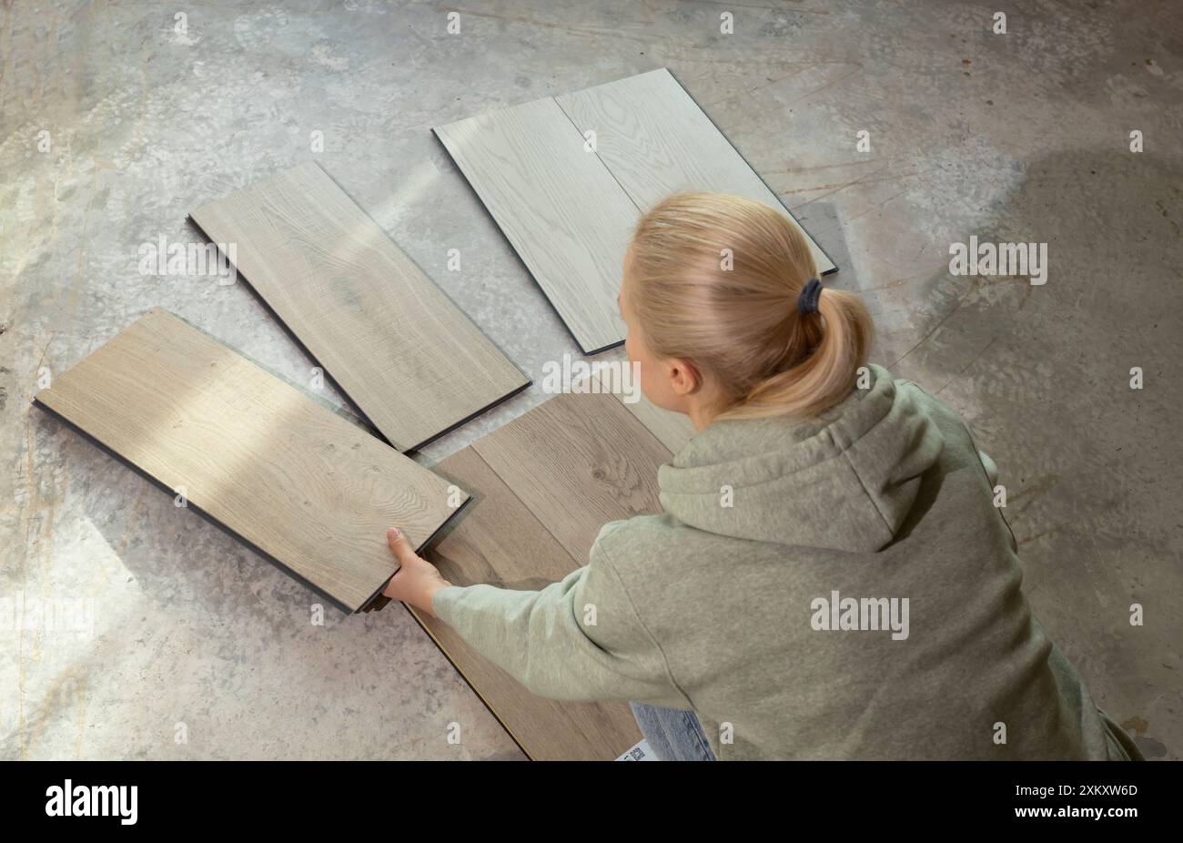 Femme détient des échantillons de bois de vinyle de luxe sur plancher de béton dans la maison. Choisir, sélectionner revêtement de sol étanche. Reconstruction de la maison. Collection de carreaux de vinyle Banque D'Images