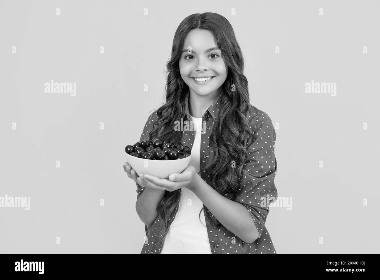 une jeune fille gaie tient un bol de cerise sur fond jaune Banque D'Images