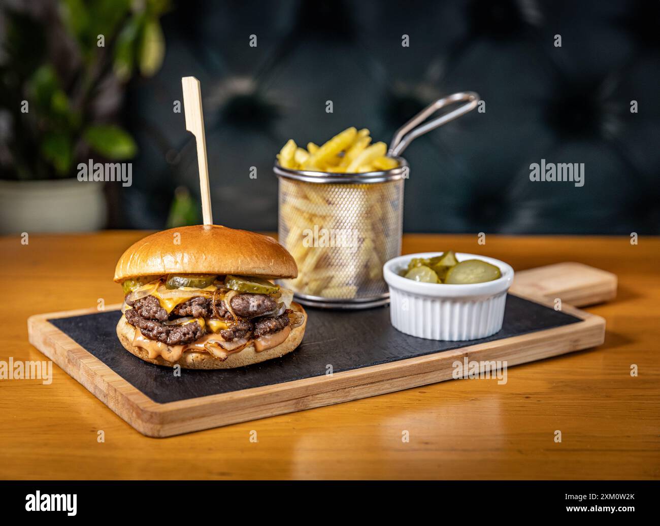 Double burger de bœuf avec fromage, cornichons et sauce est debout sur une ardoise noire avec frites et cornichons Banque D'Images
