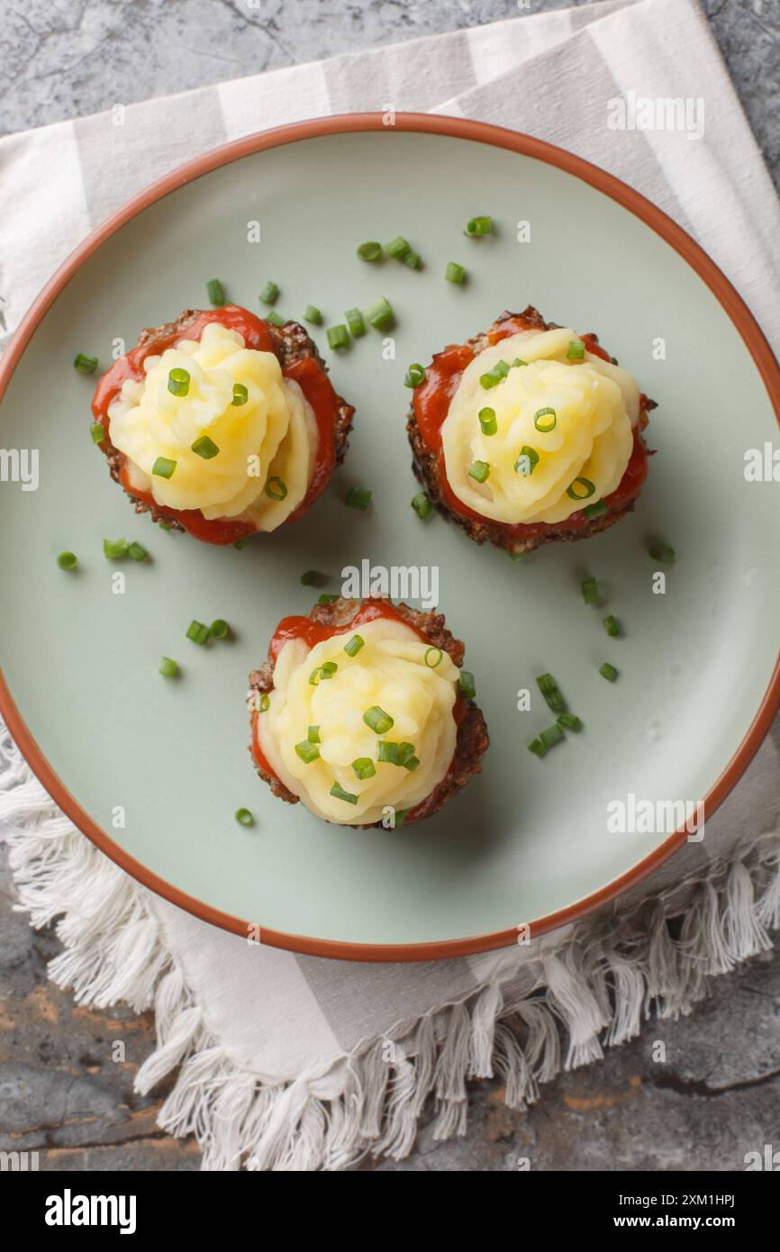 Les muffins de pain de viande sont une façon amusante de servir cette nourriture réconfortante avec de la purée de pommes de terre sur le dessus gros plan sur l'assiette sur la table. Vue de dessus verticale Banque D'Images