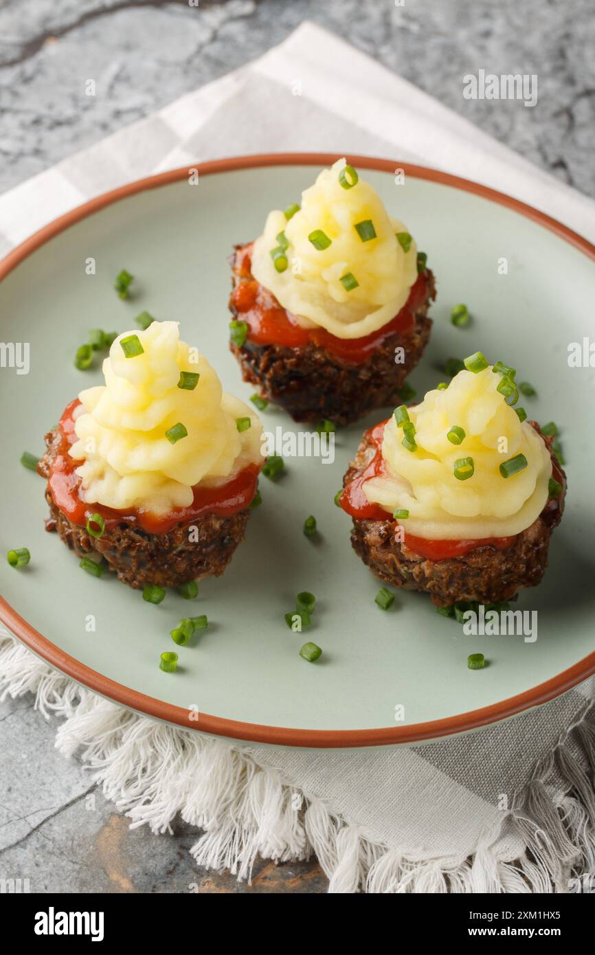 Les muffins de pain de viande sont une façon amusante de servir cette nourriture réconfortante avec de la purée de pommes de terre sur le dessus gros plan sur l'assiette sur la table. Vertical Banque D'Images