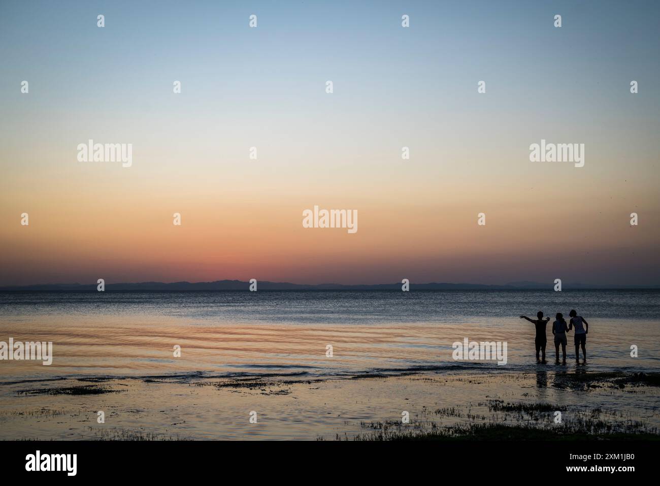 Trois personnes marchant dans l'eau au crépuscule au lac Nicaragua, île d'Ometepe, département de Rivas, Nicaragua Banque D'Images