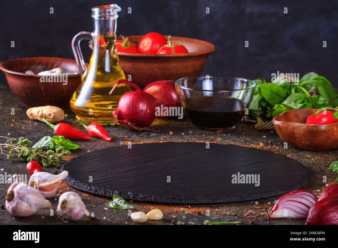 Fond culinaire avec plateau de service en pierre d'ardoise de cuisine, huile d'olive et légumes. Mise au point sélective avec espace de copie pour le texte Banque D'Images