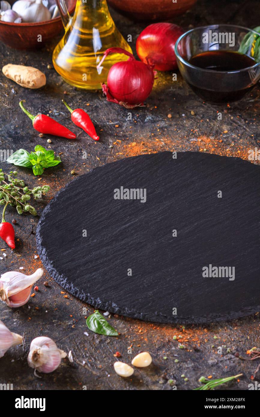 Fond culinaire avec plateau de service en pierre d'ardoise de cuisine, huile d'olive et légumes. Mise au point sélective avec espace de copie pour le texte Banque D'Images