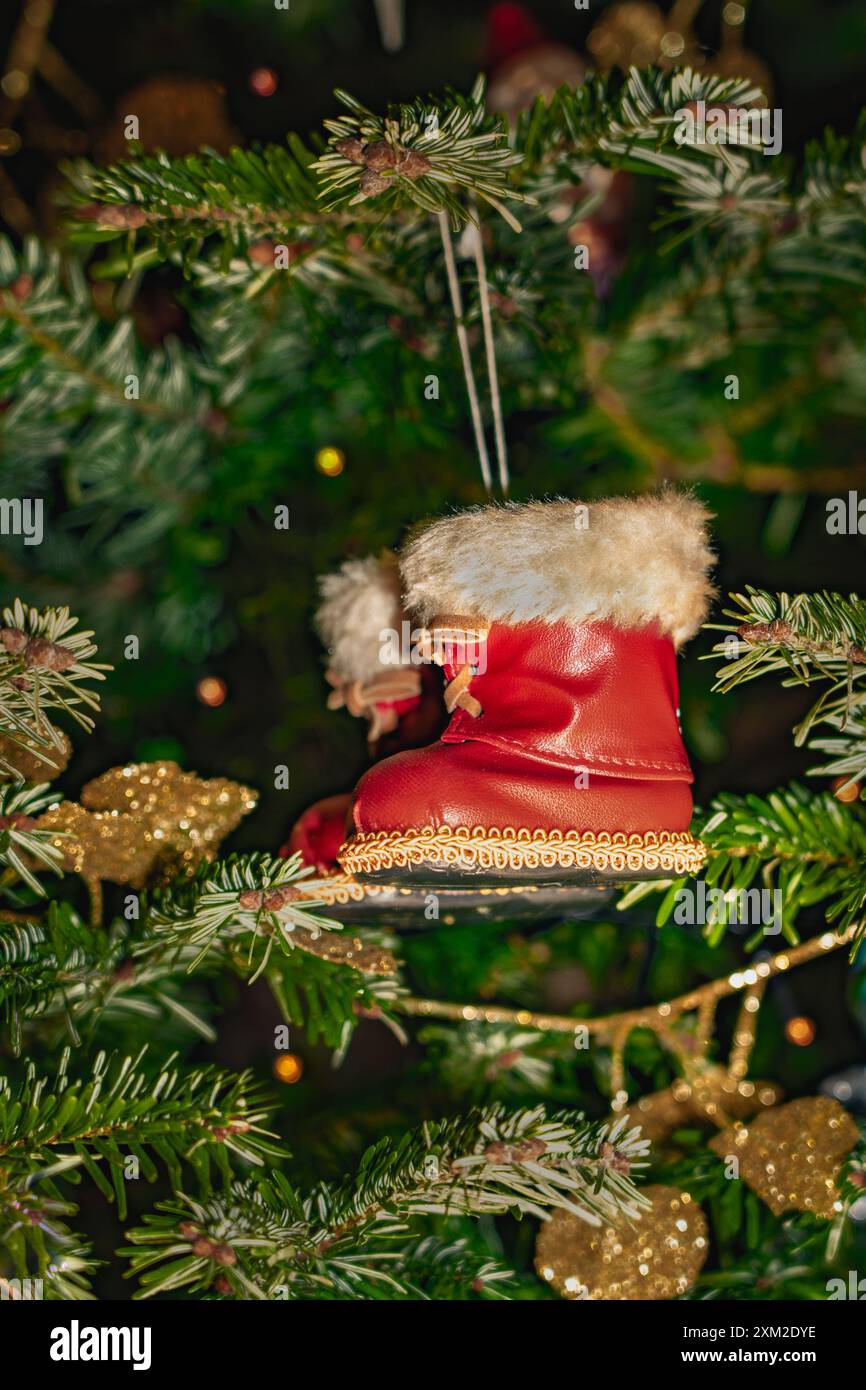 L'ornement de bottes rouges du Père Noël avec une bordure de fourrure blanche est suspendu à un arbre de Noël vert Banque D'Images