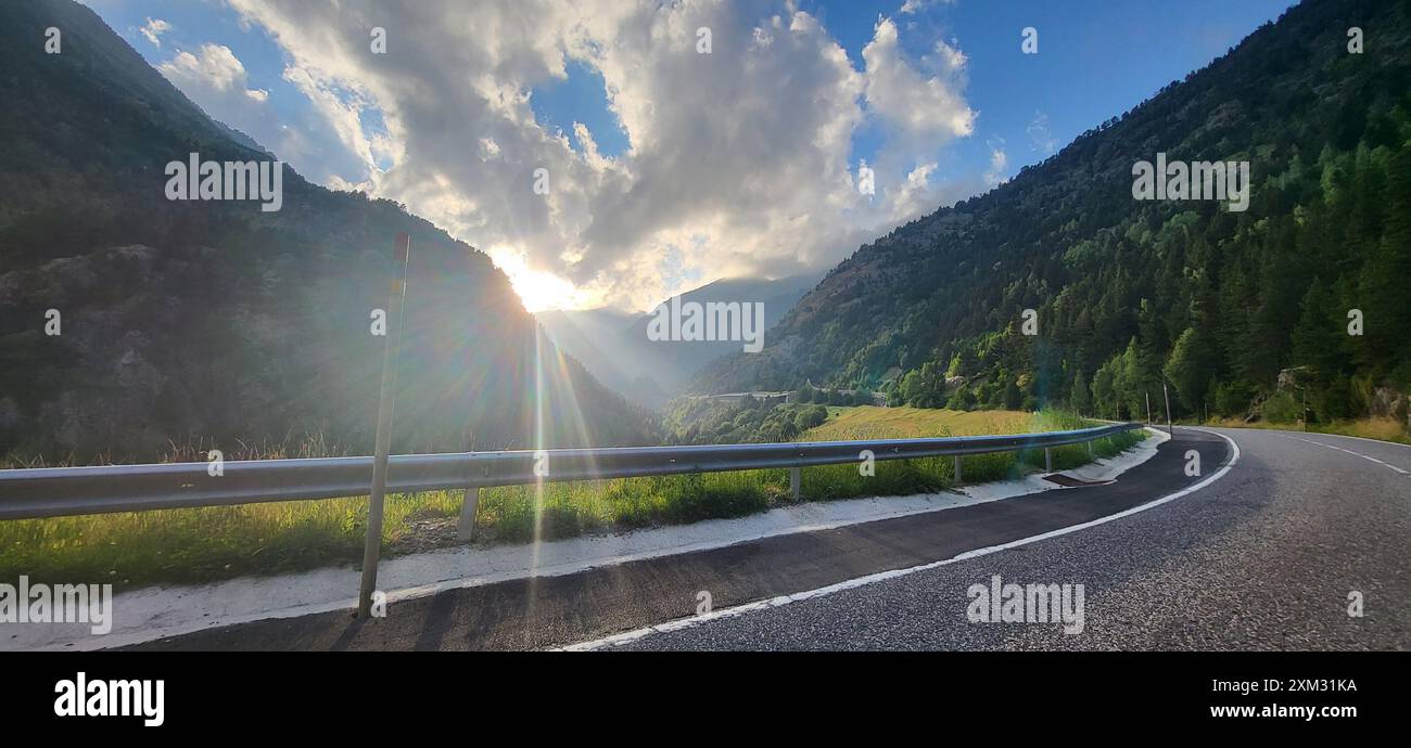 Un paysage de montagne à couper le souffle au coucher du soleil avec une route sinueuse et un ciel spectaculaire. Les rayons du soleil traversent les nuages, illuminant la vallée. Banque D'Images