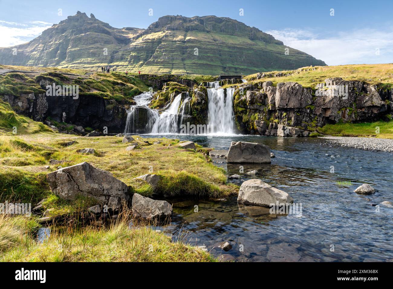 Cascade en cascade au-dessus des rochers avec montagne verte luxuriante sous ciel bleu clair Banque D'Images