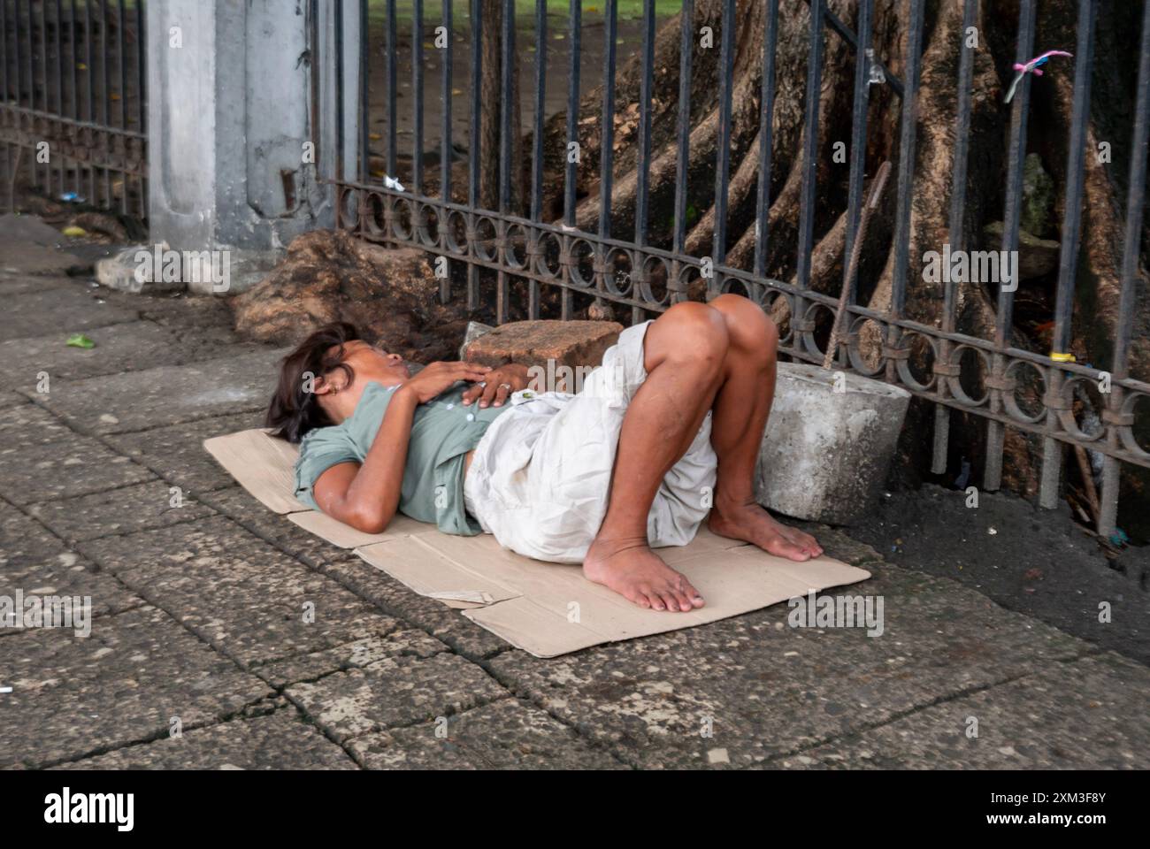 Manille, Philippines - 25 août 2019 : personne sans abri dormant sur du carton près de la clôture Banque D'Images