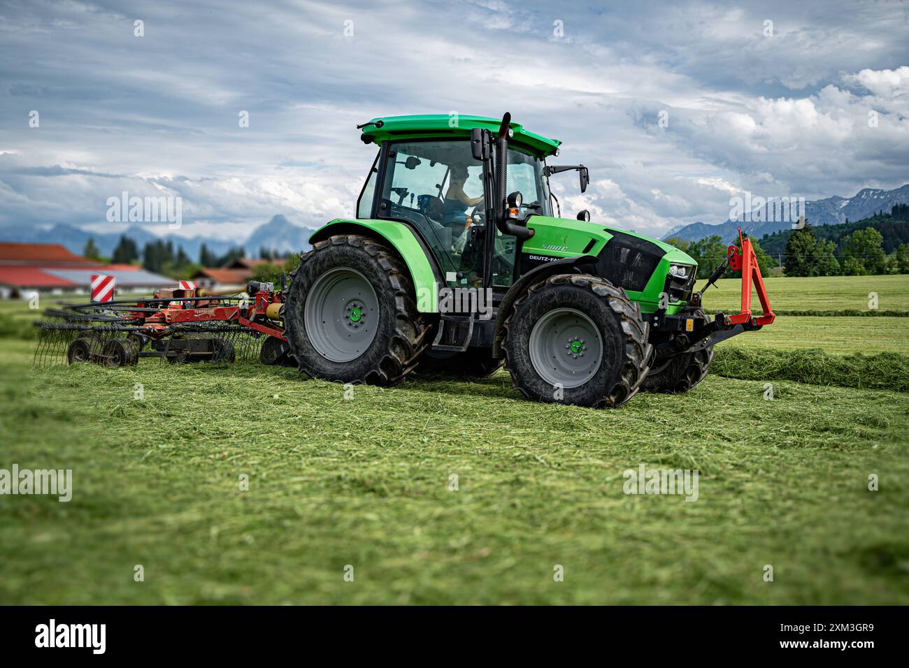 Grünfuttergewinnung im Allgäu - Deutz-Fahr Traktor mit Heuschwader beim gras schwaden. IM Allgäu erzeugen viele Bauern auch die sogenannte Heumilch. Dabei darf an die Milchkühe keine Silage - weder gras- noch Maissilage verfüttert werden. Oftmals sind kleinere Käsereien angeschlossen, der Käse wird direkt vermarktet. Der Ausschluss von Silagefütterung verhindert, dass die Milch den Strengen Geschmack der Silage annimmt. Oberallgäu Bayern Deutschland *** production de fourrage vert dans le tracteur Allgäu Deutz Fahr avec un râteau à foin andainant l'herbe dans le Allgäu, de nombreux agriculteurs produisent également ce que l'on appelle le foin M. Banque D'Images