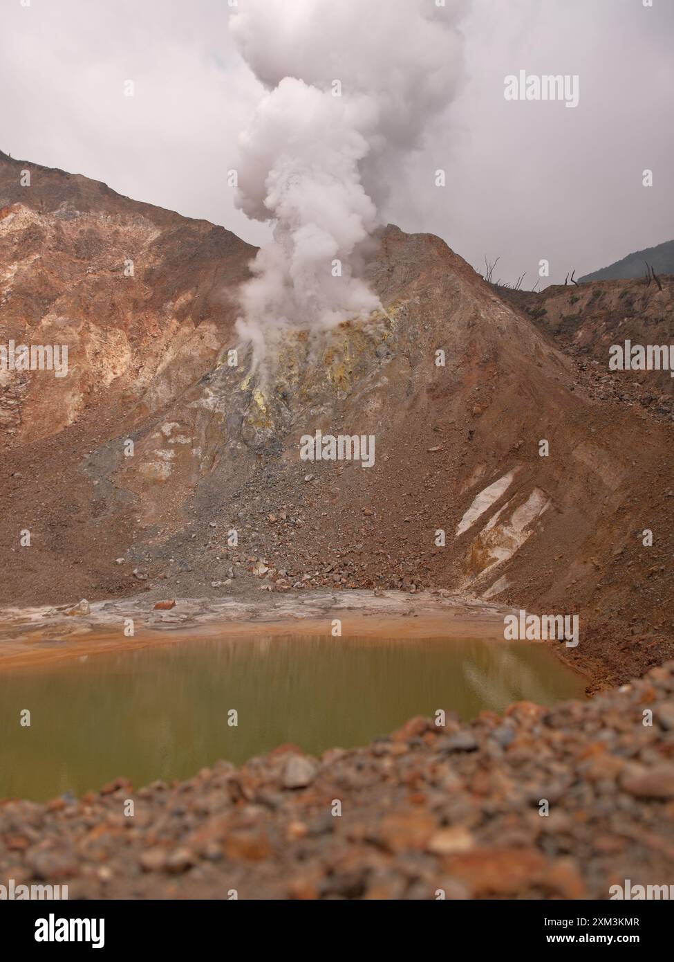 Une grande montagne avec un grand trou sur le côté et une grande masse d'eau. L'eau est verte et la montagne est couverte de rochers Banque D'Images