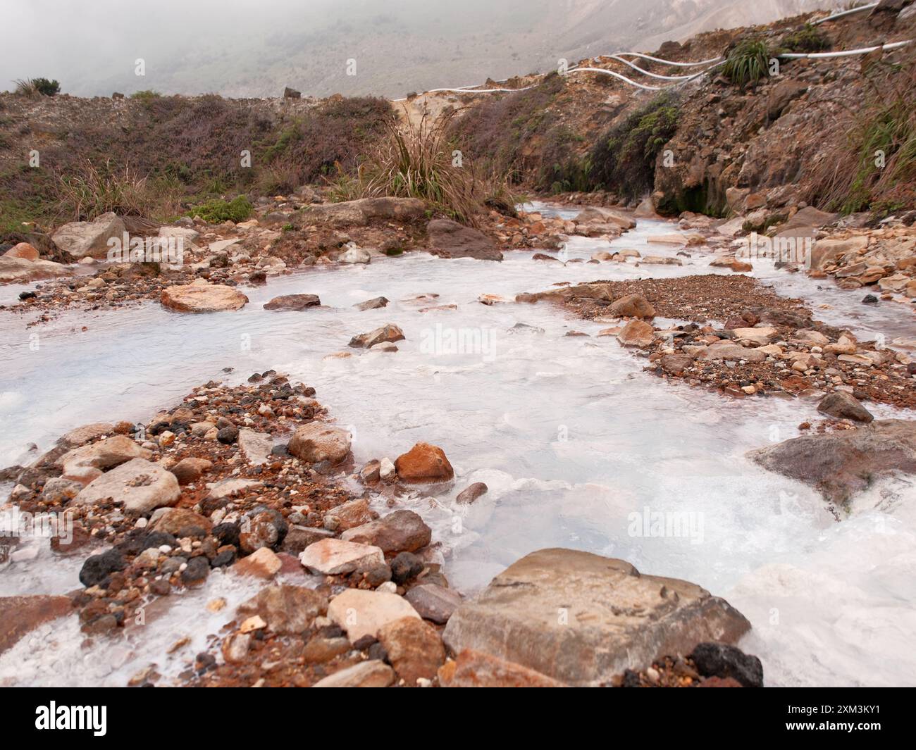 Une rivière rocheuse avec une substance blanche coulant à travers elle. L'eau est trouble et les rochers sont dispersés dans toute la rivière. La scène est désolée an Banque D'Images