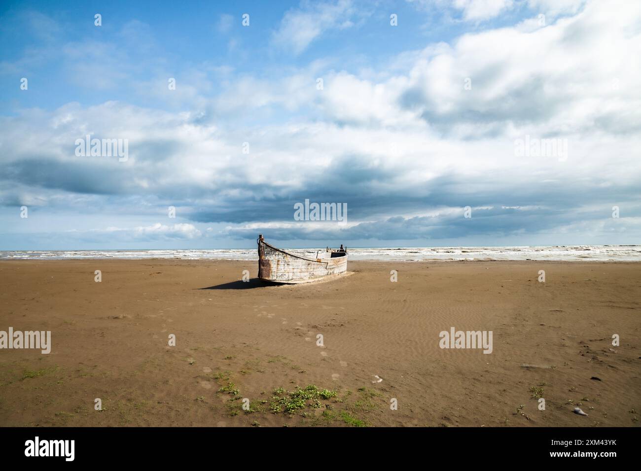 Bateau de pêche en bois abandonné sur la rive sablonneuse de la mer Caspienne contre le ciel nuageux Banque D'Images