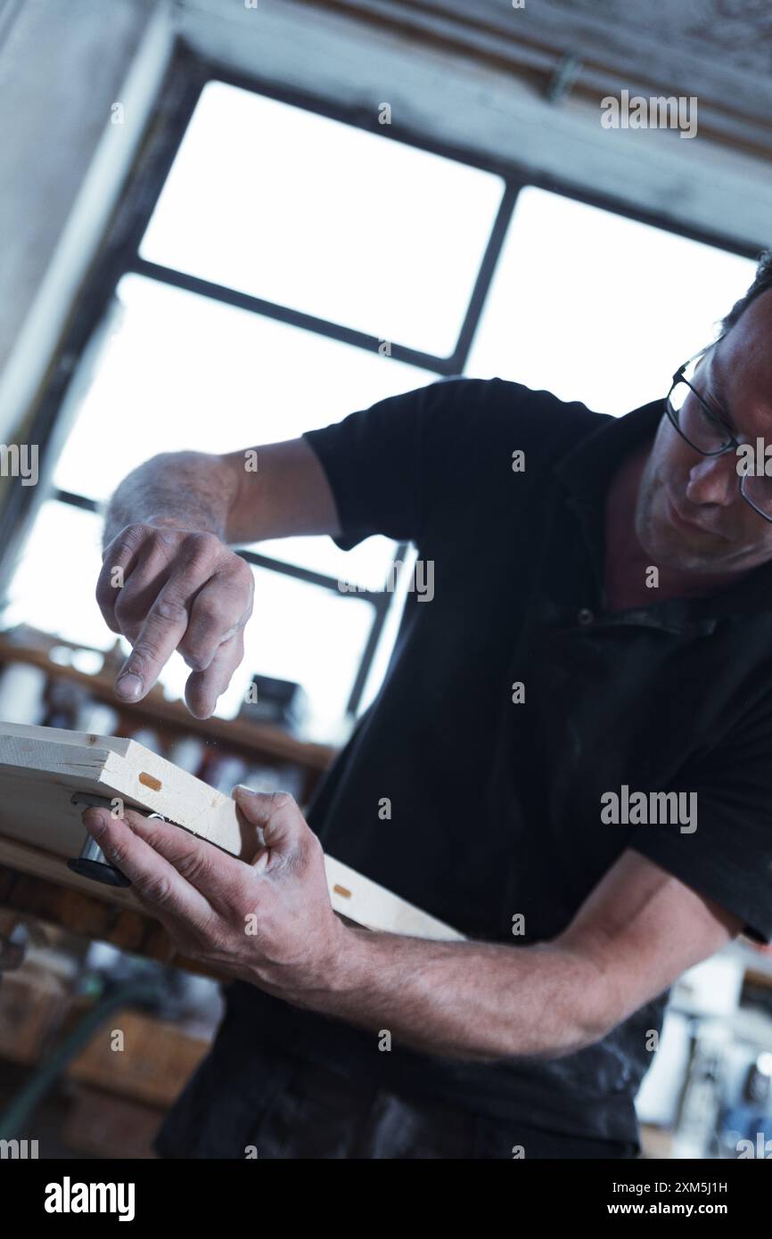 Menuisier qualifié fabriquant des meubles personnalisés dans un atelier de bois confortable avec des outils traditionnels, mettant en valeur la passion et l'expertise dans le travail du bois Banque D'Images