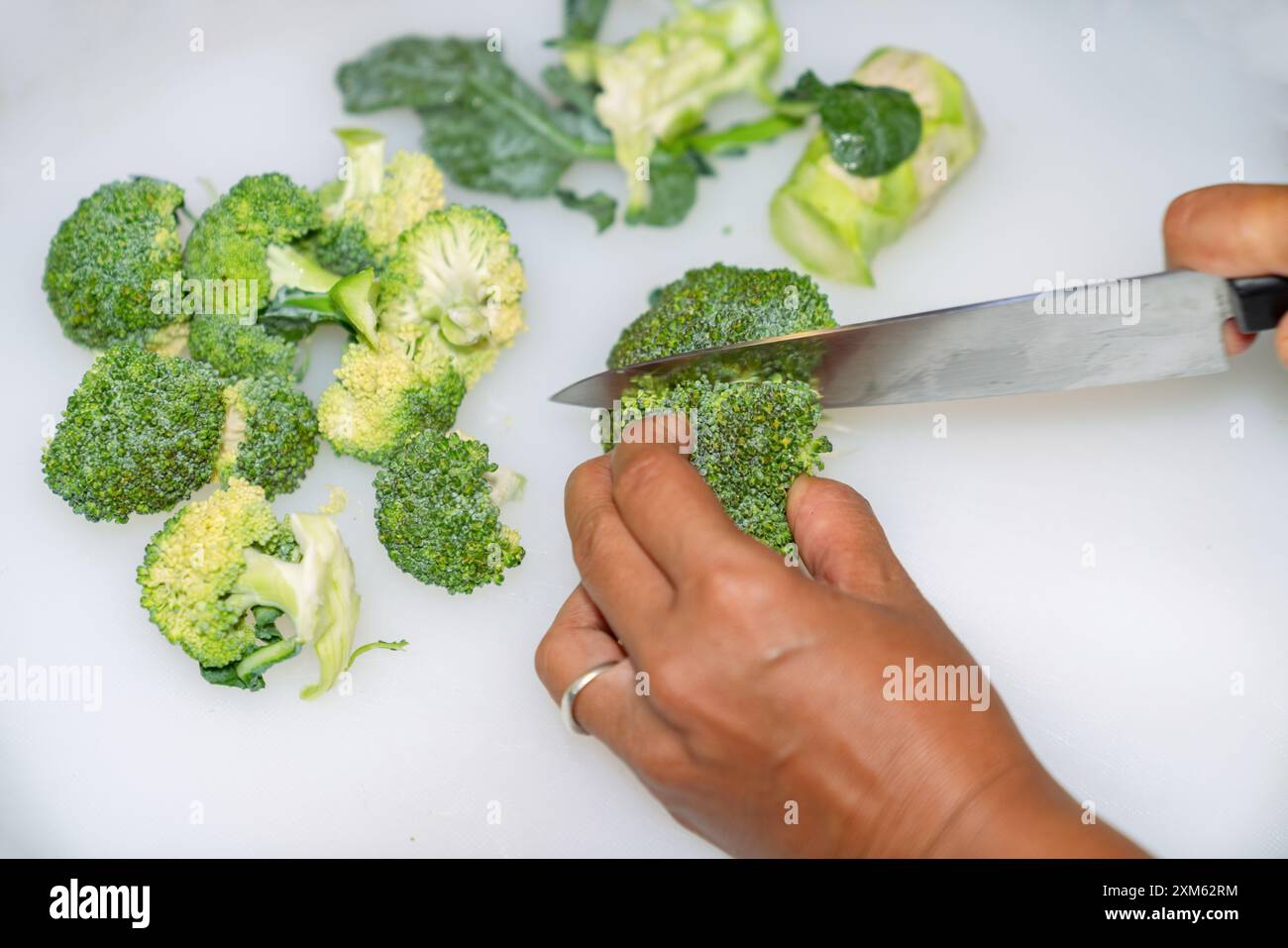 Fermez la main de la femme coupant le brocoli sur une planche à découper blanche dans la cuisine pour cuisiner. Banque D'Images