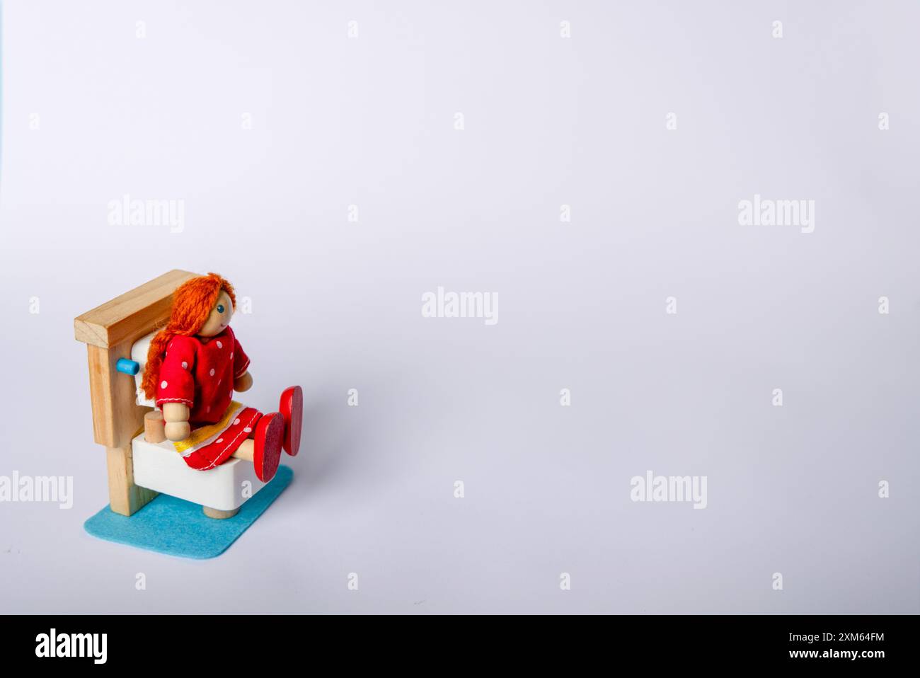 Une fille jouet en bois assise sur une toilette, placée sur un fond blanc. Cette représentation mignonne et originale capture une routine quotidienne commune Banque D'Images