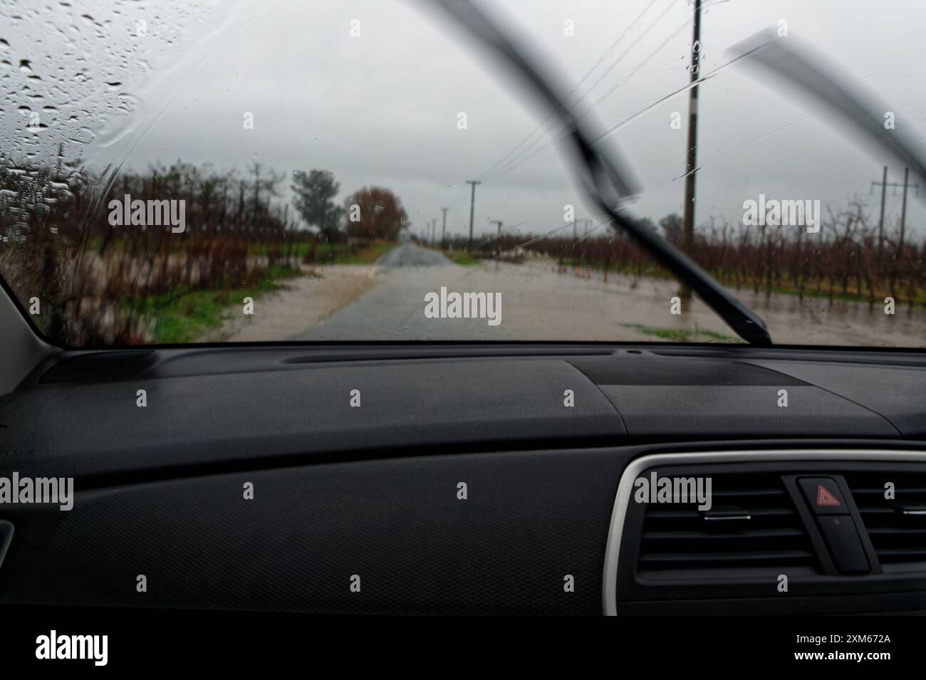 Les essuie-glaces se mettent en marche lorsqu'une voiture à conduite à droite approche d'une section de route inondée. Banque D'Images Les essuie-glaces se mettent en marche lorsqu'une voiture à conduite à droite approche d'une section de route inondée. Banque D'Images