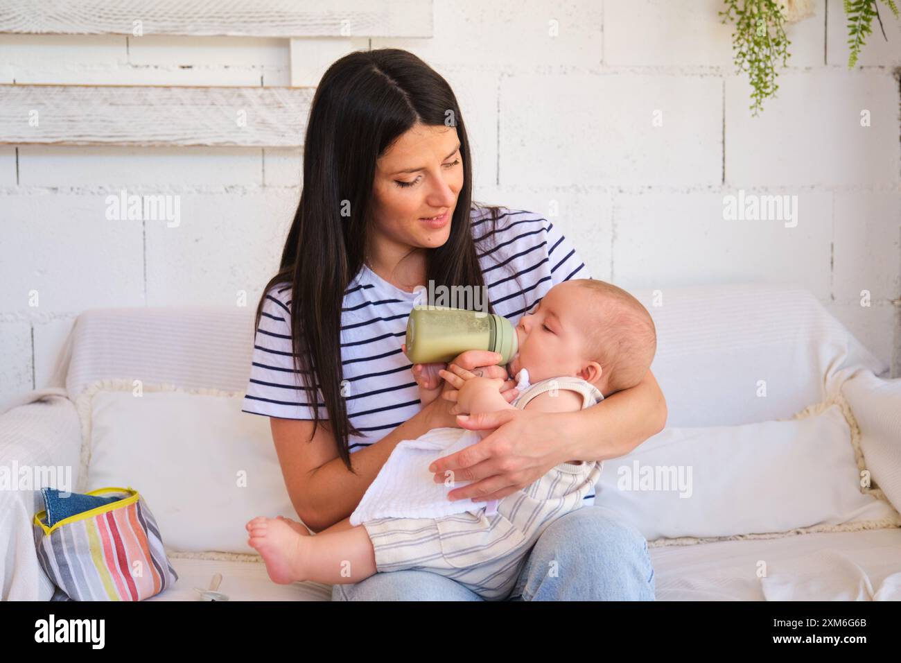Mère attentionnée nourrissant son fils bébé avec un biberon sur un canapé Banque D'Images