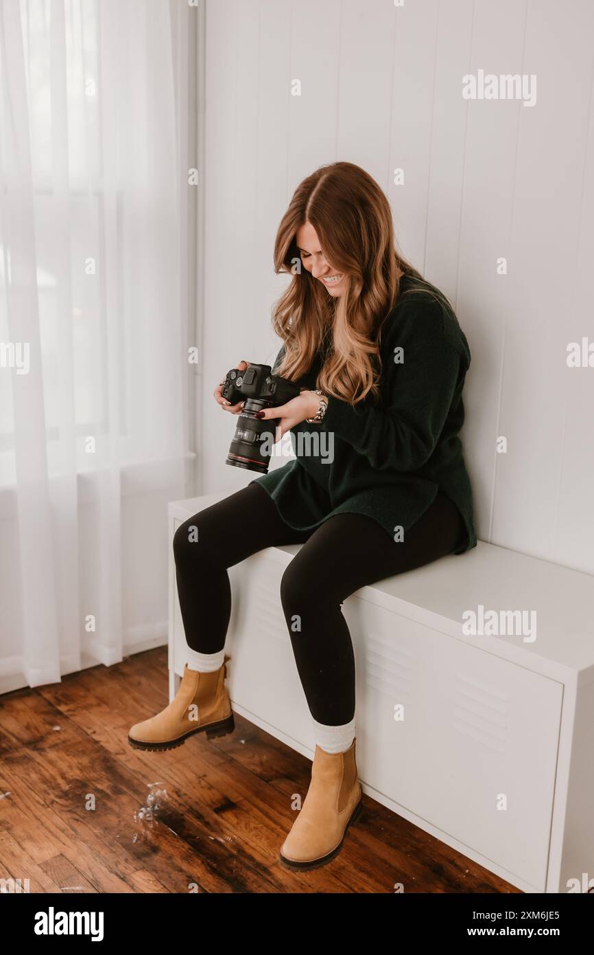 Femme souriante tenant un appareil photo, assise sur une armoire blanche Banque D'Images