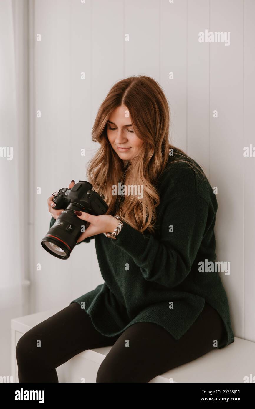 Femme souriante tenant une caméra, assise dans une pièce lumineuse Banque D'Images