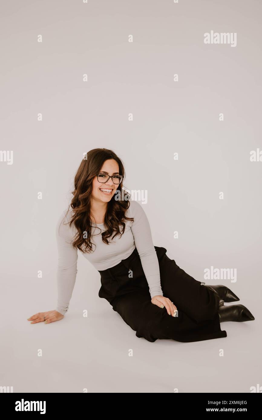 Jeune femme hispanique assise sur le sol, souriante, fond blanc Banque D'Images