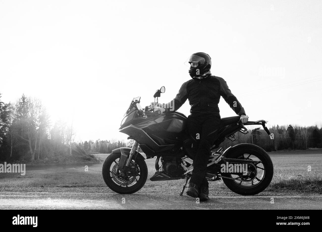 Homme debout avec sa moto sur une route de campagne suédoise Banque D'Images