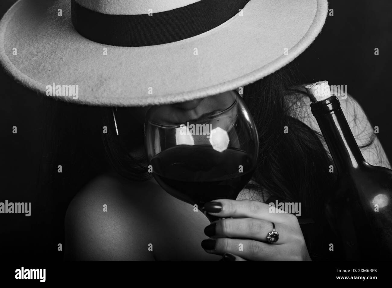 Portrait en gros plan noir et blanc d'une femme portant un chapeau buvant du vin dans une tasse en verre. Photo studio. Banque D'Images