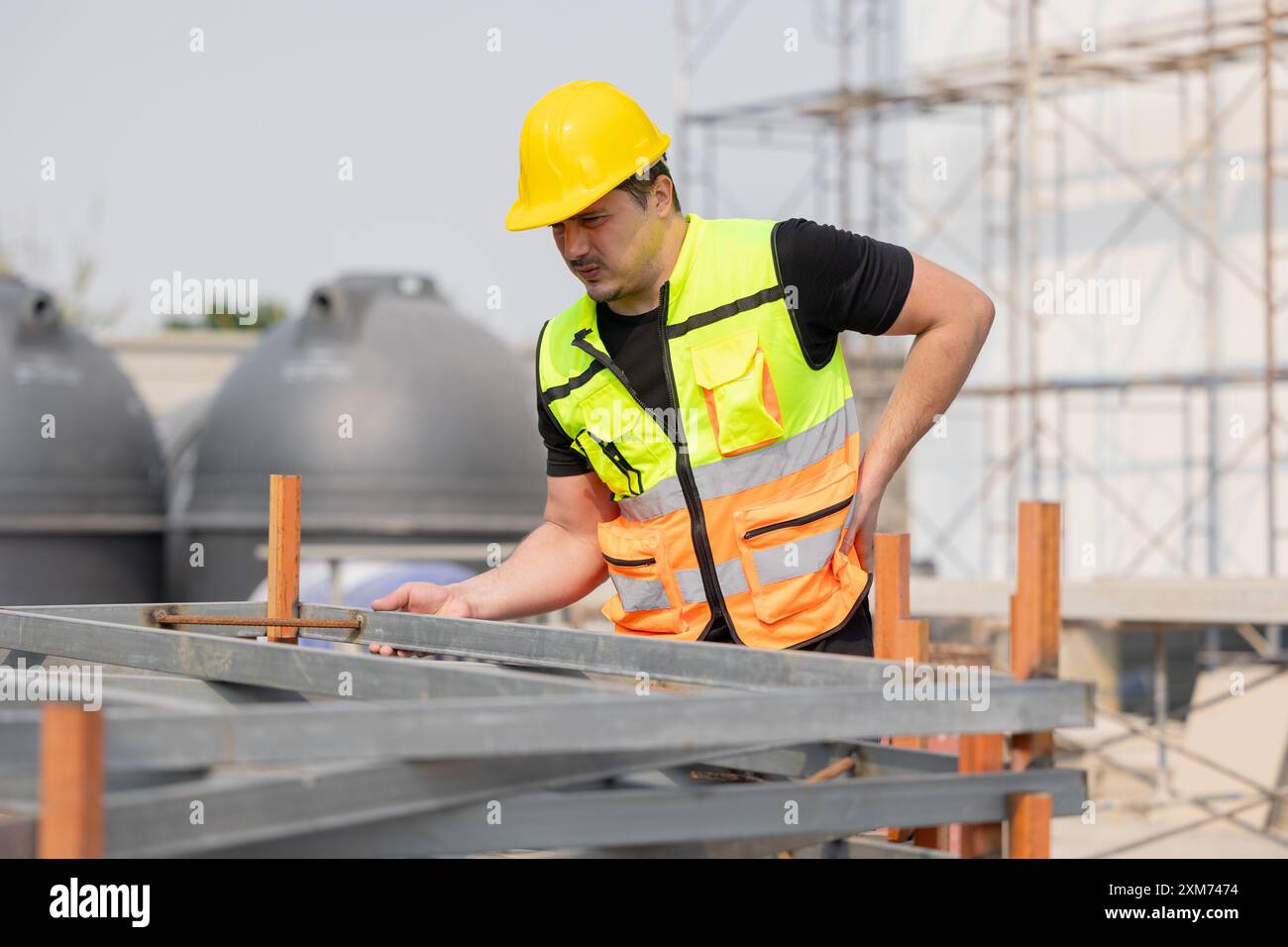 Travailleur de la construction en gilet de sécurité et casque de sécurité inspectant la structure sur le chantier de construction, éprouvant des douleurs lombaires. Concept de santé au travail et Banque D'Images