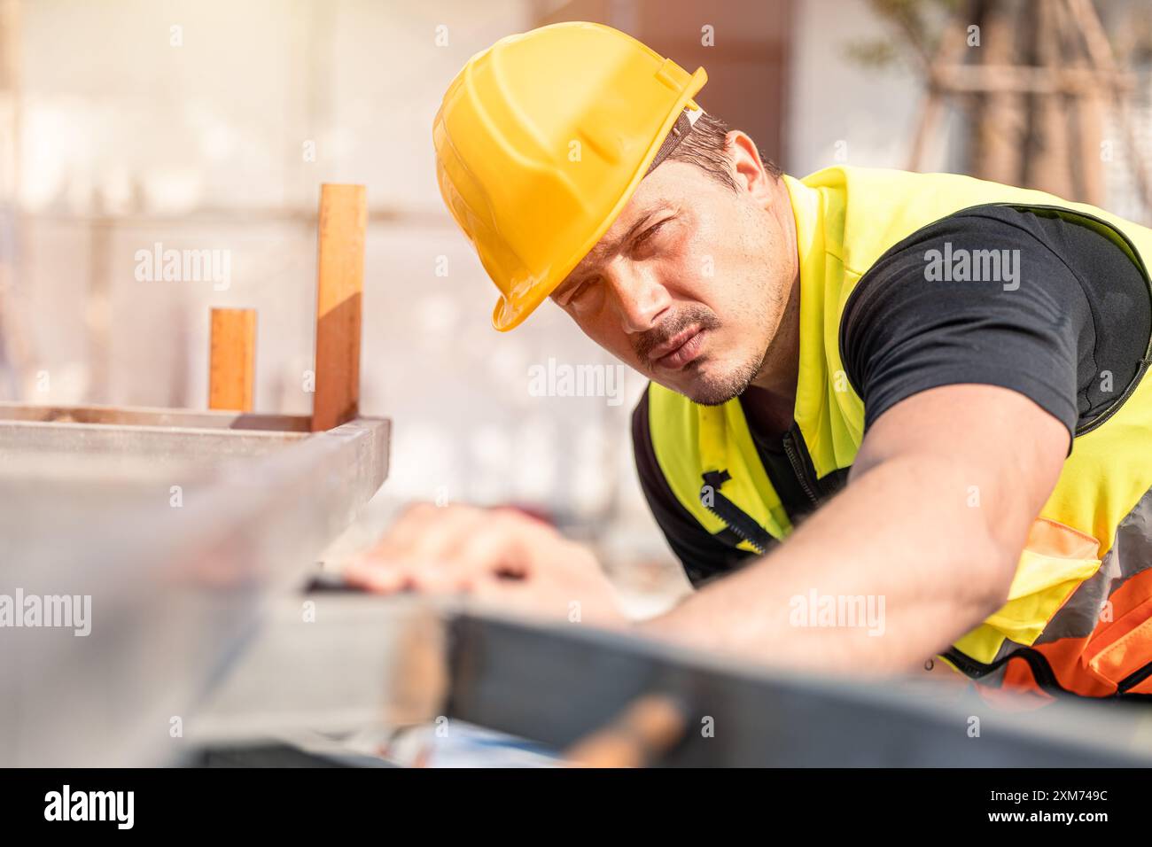 Un travailleur de la construction dévoué portant un casque de sécurité jaune et un gilet de sécurité se concentre sur sa tâche sur un chantier de construction. Banque D'Images