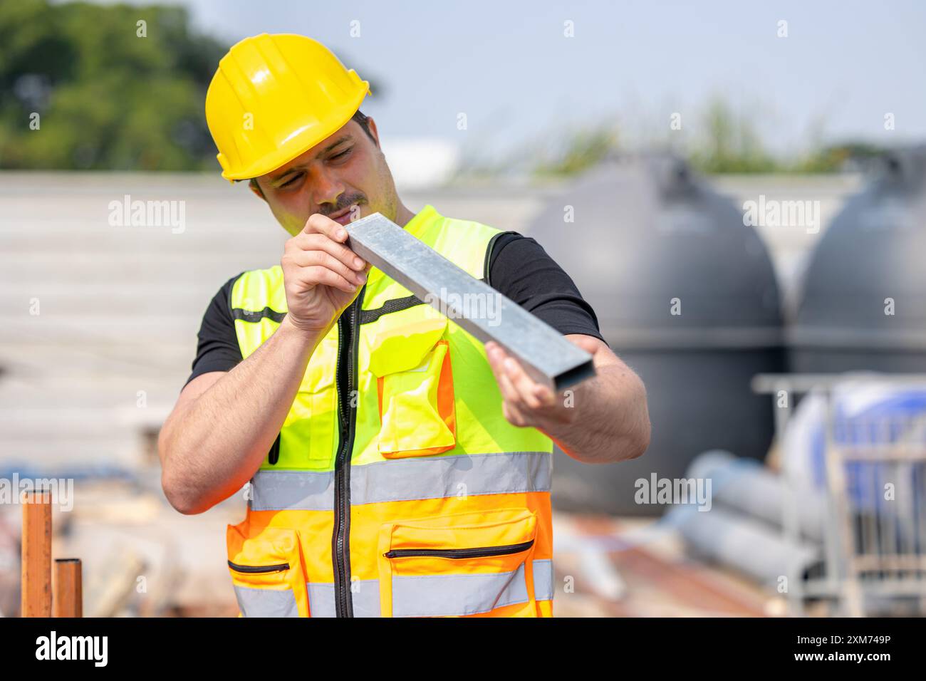 Un travailleur de la construction dévoué portant un casque de sécurité jaune et un gilet de sécurité se concentre sur sa tâche sur un chantier de construction. Banque D'Images