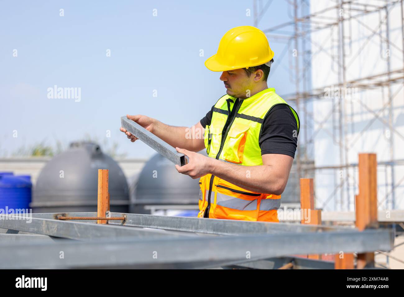 Un travailleur de la construction dévoué portant un casque de sécurité jaune et un gilet de sécurité se concentre sur sa tâche sur un chantier de construction. Banque D'Images