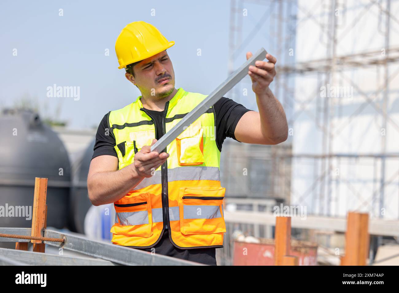 Un travailleur de la construction dévoué portant un casque de sécurité jaune et un gilet de sécurité se concentre sur sa tâche sur un chantier de construction. Banque D'Images