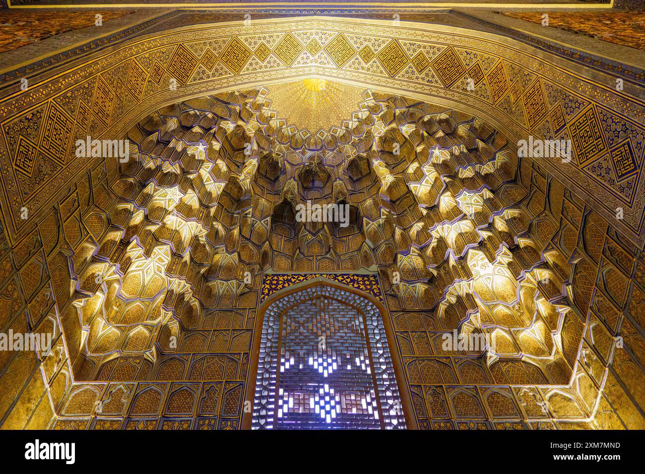 Plafond muqarnas richement décoré avec des motifs géométriques à l'intérieur d'une structure architecturale islamique avec lumière ambiante incandescente Banque D'Images
