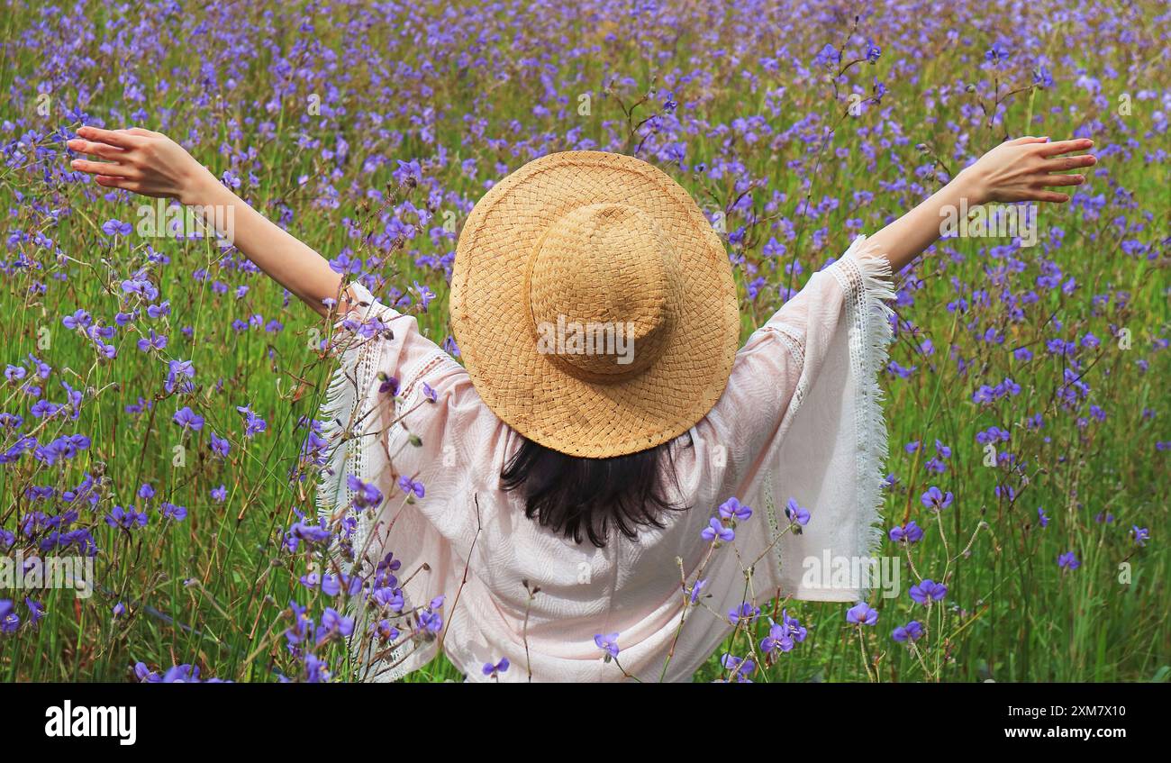 Femme heureuse levant les bras dans un magnifique champ de fleurs Murdannia gigantea Banque D'Images