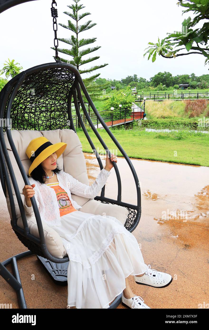 Femme se relaxant sur une chaise pivotante en rotin à la terrasse après la pluie Banque D'Images