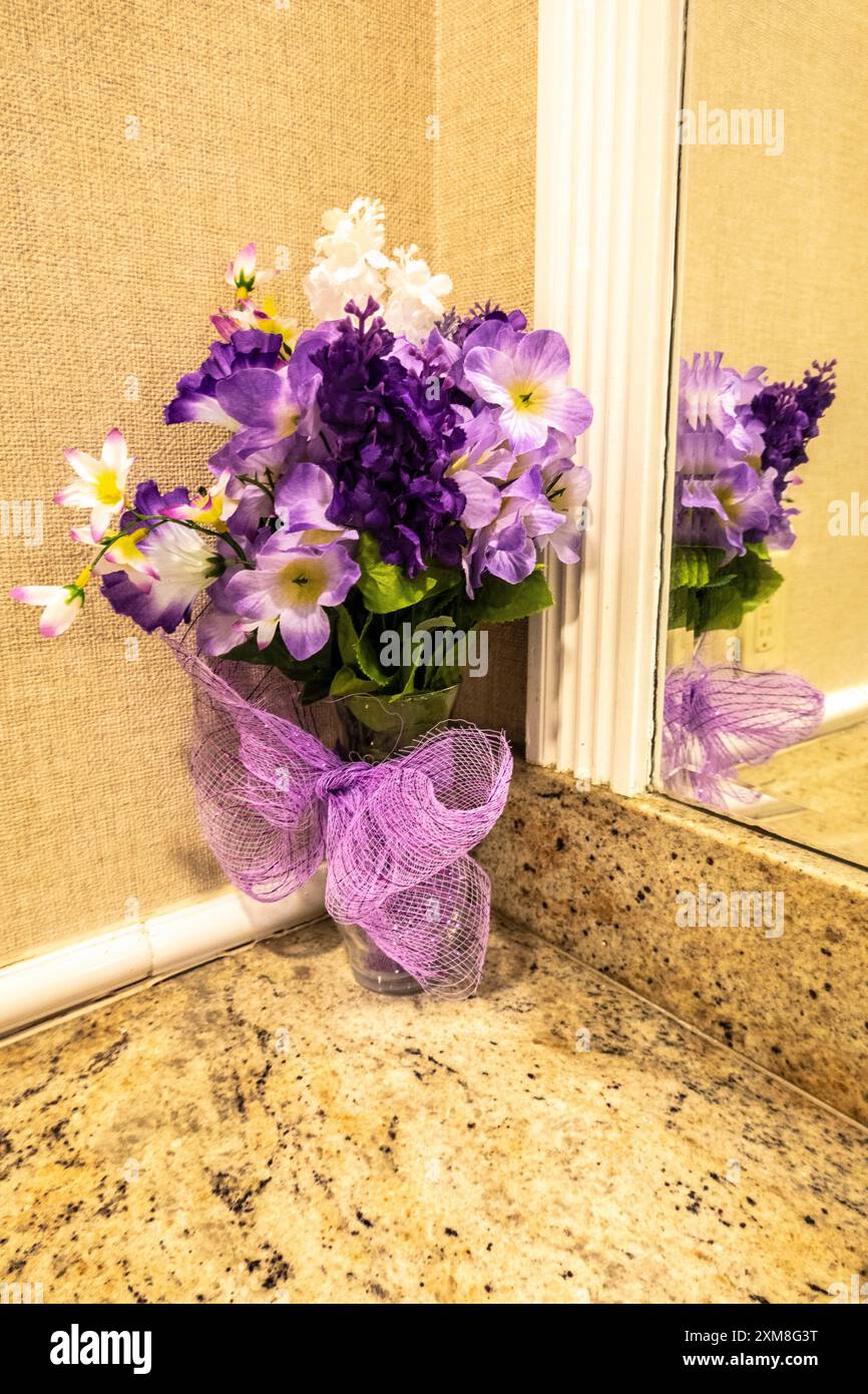 Fleurs artificielles roses et violettes dans un vase reflété dans le miroir sur le comptoir en marbre d'une chambre de dames Banque D'Images