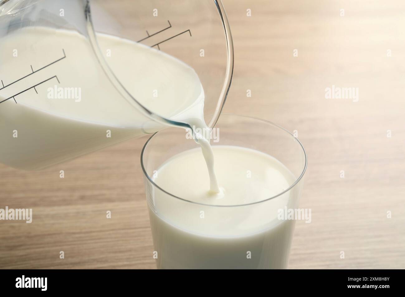 Verser le lait frais de la cruche dans le verre à la table en bois, gros plan Banque D'Images