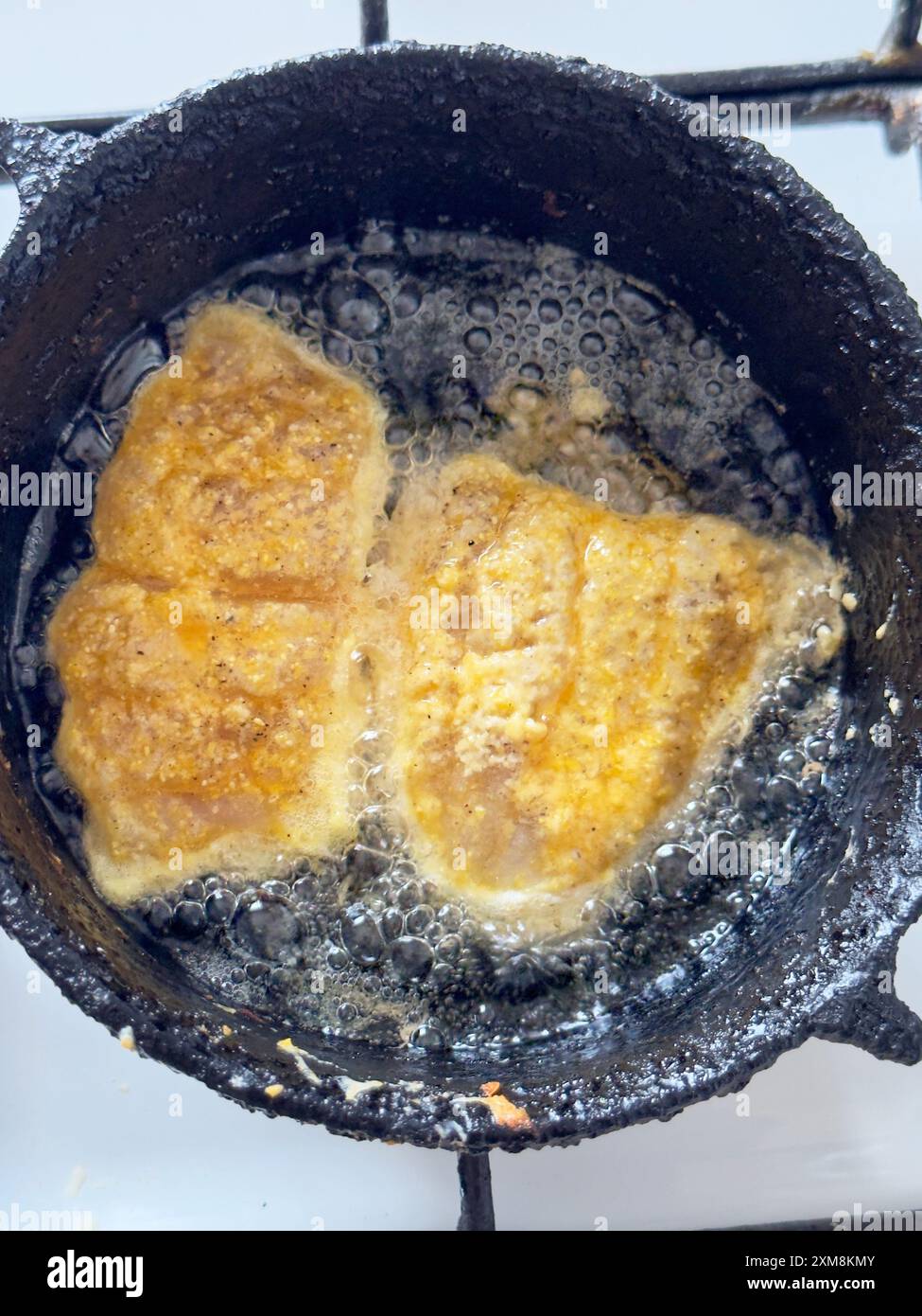 Gros plan de deux morceaux de poisson frit cuisant dans une poêle en fonte Banque D'Images