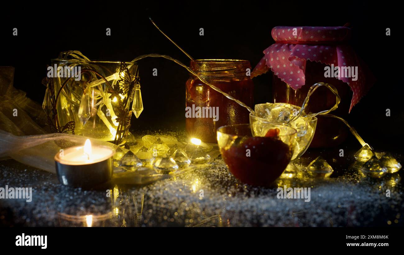 Verres avec marmelade de prunes maison, lumières de fées, bougie, cristaux de verre. Sensation d'automne atmosphérique, Banque D'Images