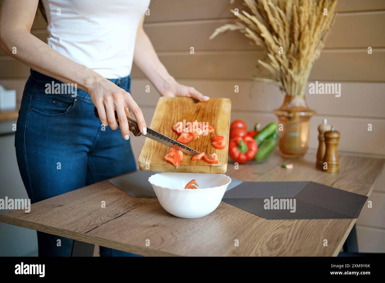 Vue rapprochée d'une femme méconnaissable versant des tomates hachées dans un bol à partir d'une planche à découper en bois Banque D'Images
