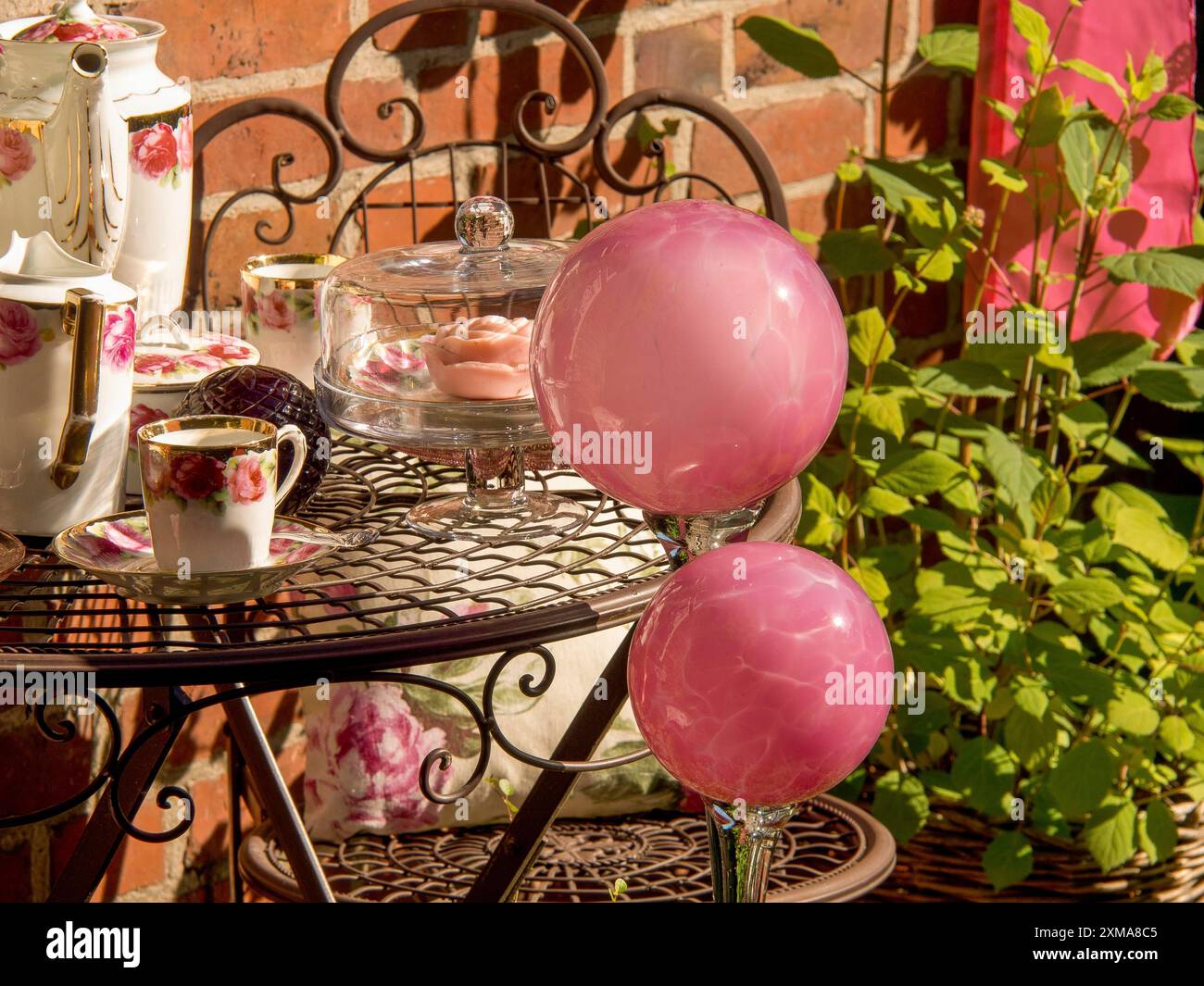 Une table dans le jardin avec service de thé floral, cloche en verre et beignets roses, entouré de plantes et mur de briques, borken, westphalie, allemagne Banque D'Images