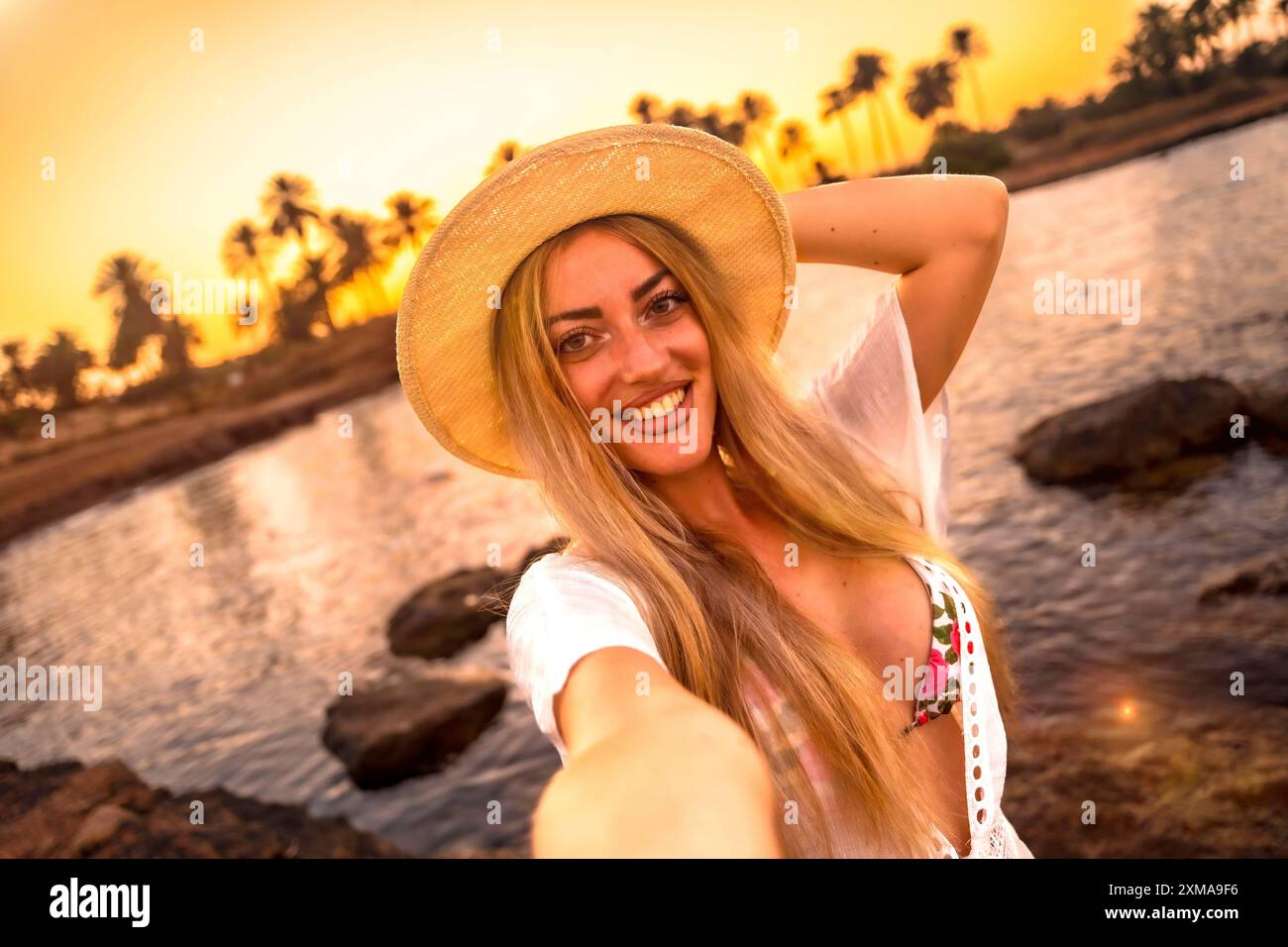 Point de vue personnel d'une femme blonde prenant un selfie pendant le coucher du soleil sur une plage tropicale Banque D'Images