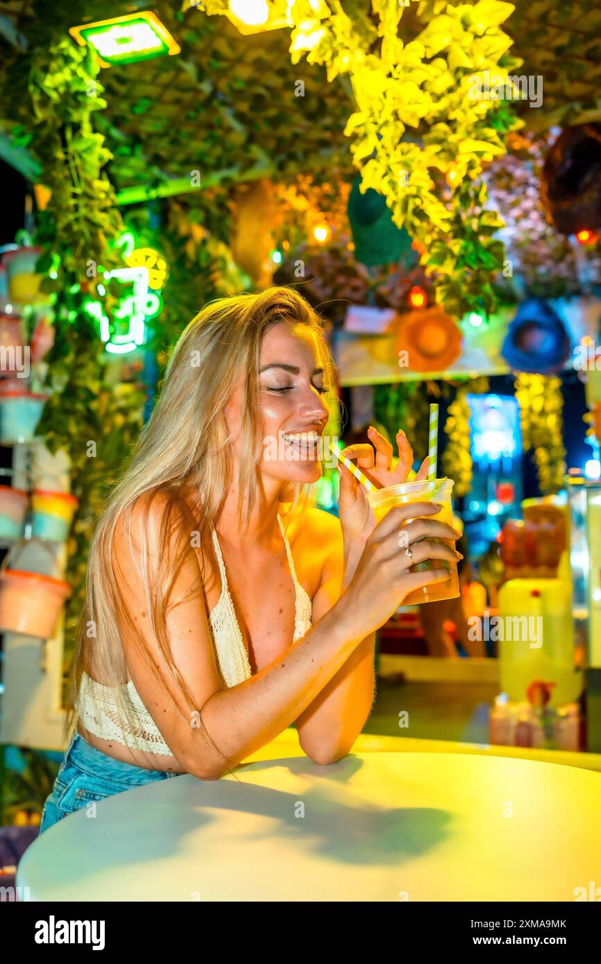Photo verticale d'une femme blonde sucant de la paille buvant un cocktail dans un bar Banque D'Images