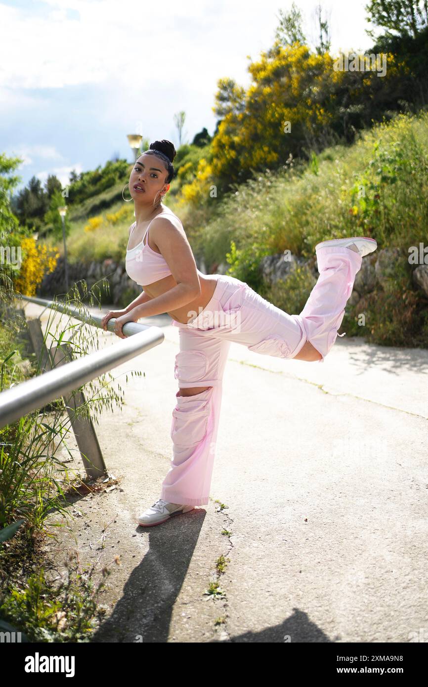 Une femme en pantalon rose pose pour une photo. Elle porte un débardeur et a ses jambes écartées. L'image a une ambiance décontractée et détendue, avec Banque D'Images