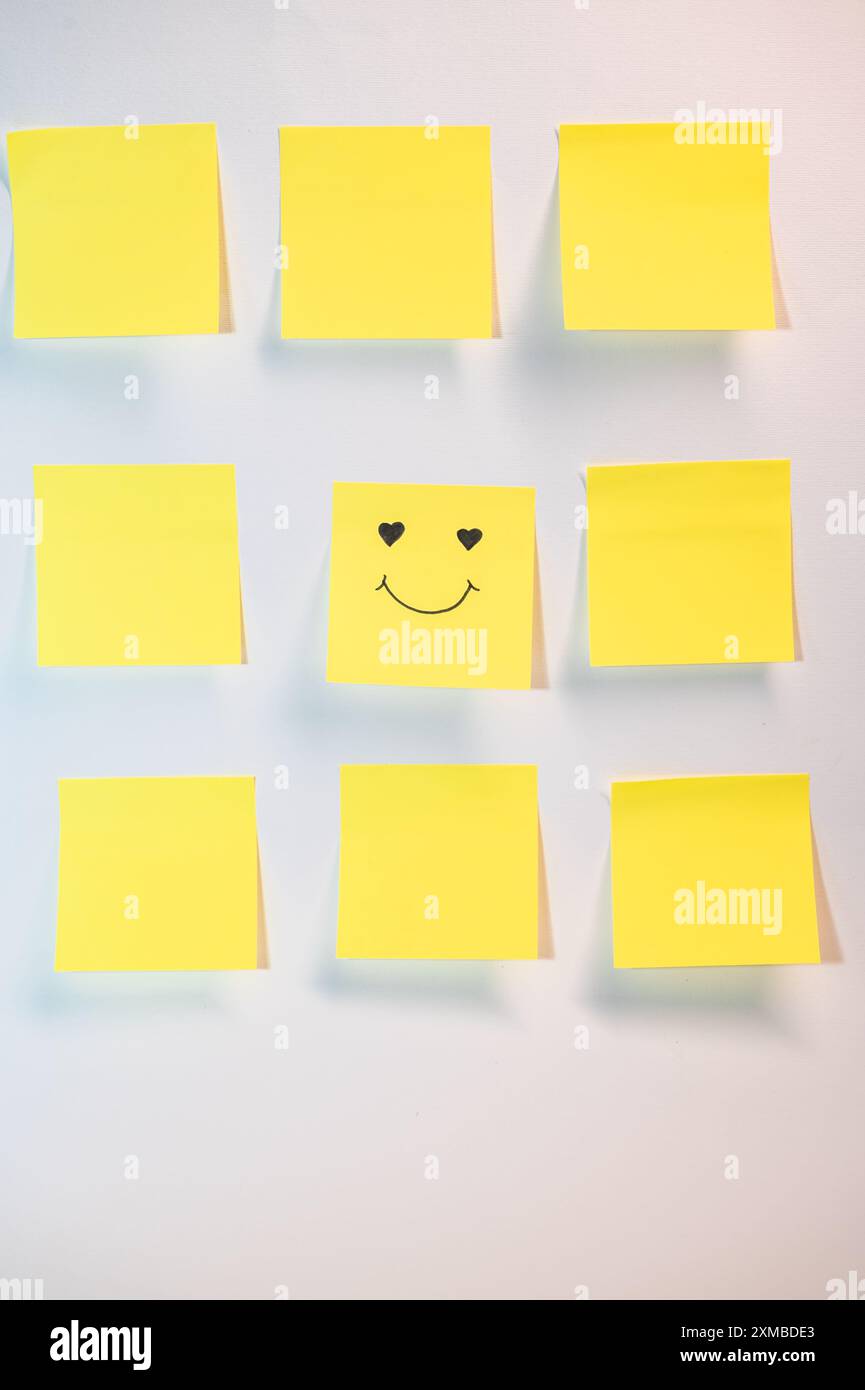 Un post jaune avec un visage souriant dessus. Il y a neuf autres post jaunes c'est sur fond blanc Banque D'Images