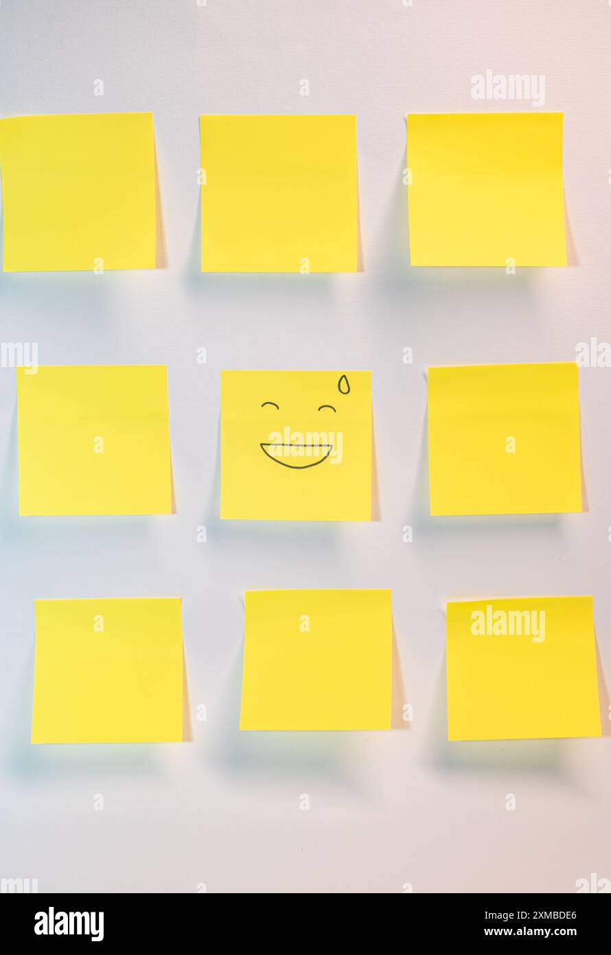 Un post jaune avec un visage souriant dessus. Il y a neuf autres post jaunes c'est sur fond blanc Banque D'Images