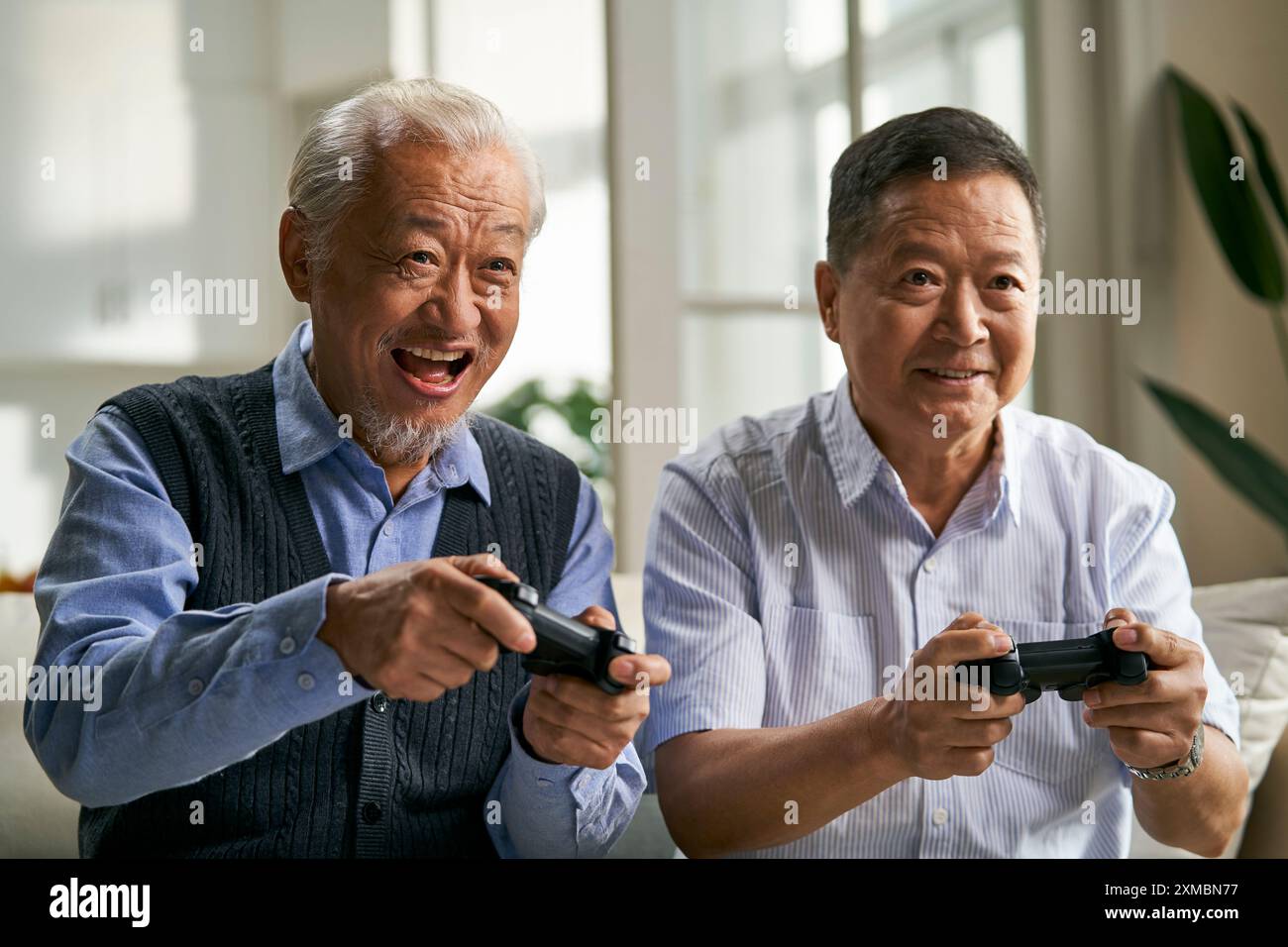 deux heureux hommes asiatiques seniors assis sur le canapé à la maison jouant au jeu vidéo Banque D'Images