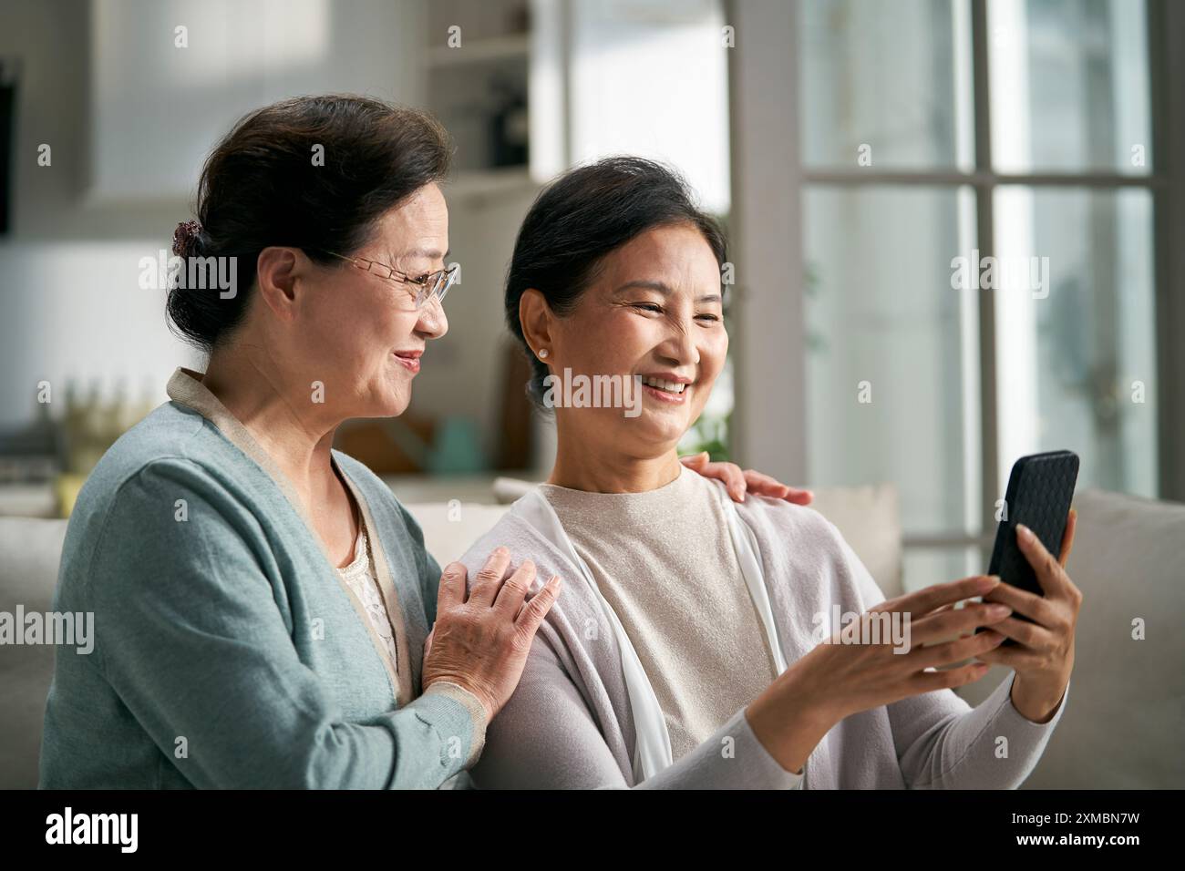 deux femmes asiatiques âgées heureuses assis sur le canapé à la maison regardant des photos de téléphone portable ensemble heureux et souriant Banque D'Images