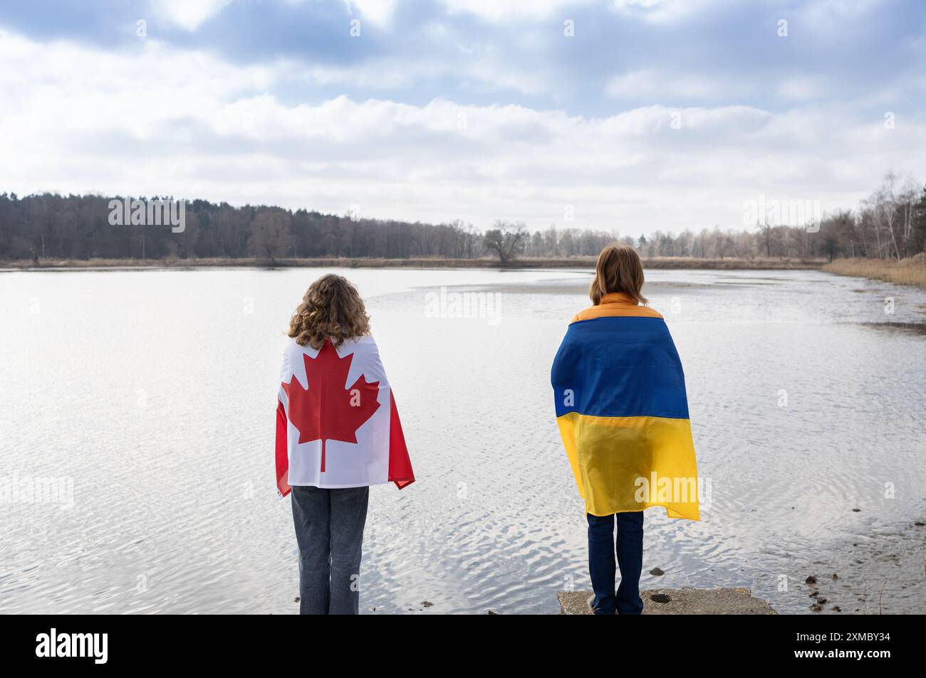 Deux femmes enveloppées de drapeaux ukrainiens et canadiens se tiennent dos à dos dans la nature. Soutien international pour l'aide à l'Ukraine pour gagner th Banque D'Images